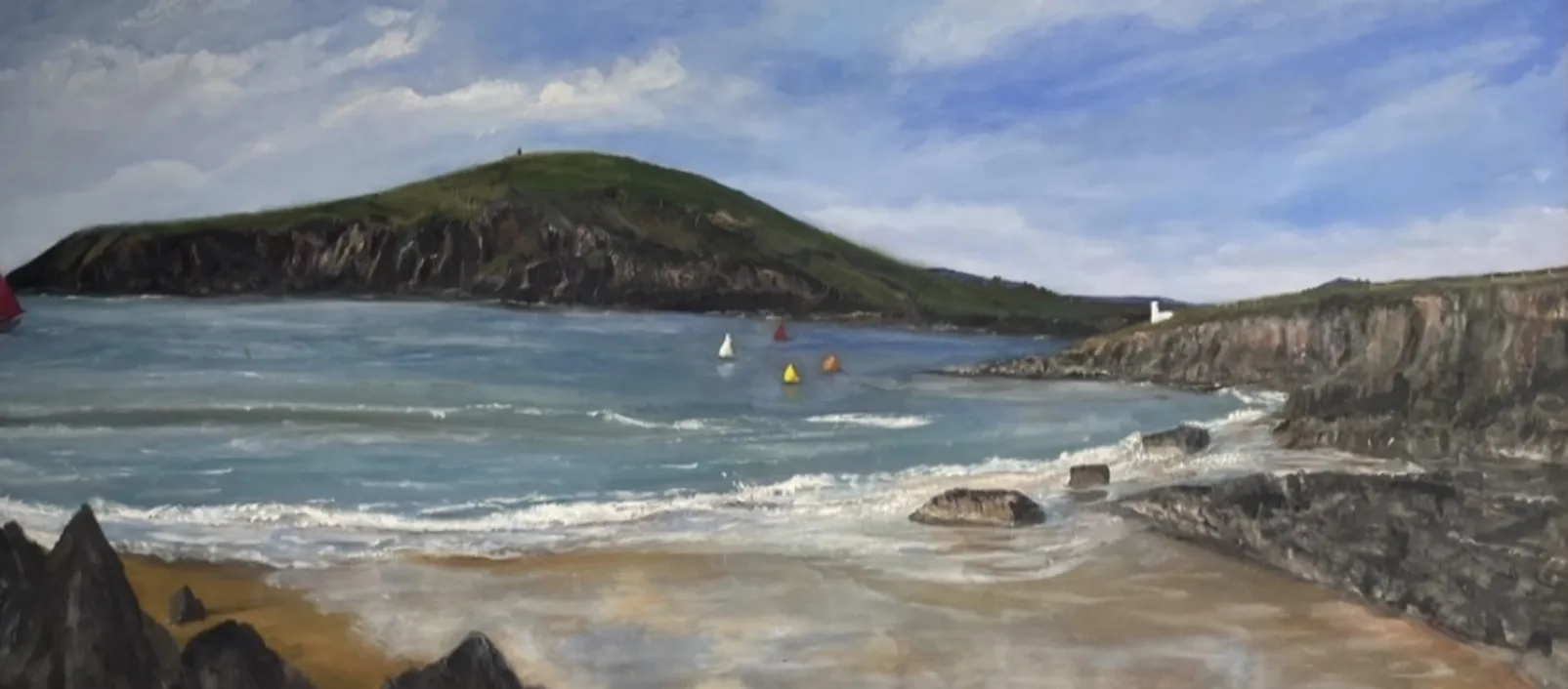 A scenic painting of a coastal landscape featuring a sandy beach with rocks in the foreground, gentle waves, and a calm sea. A few sailboats float in the water, and a green hill rises in the background under a partly cloudy sky.