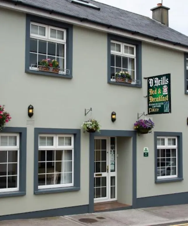 The image shows the exterior of O'Neills Bed & Breakfast, a two-story building with gray and white walls. It has multiple windows with flower boxes and a signboard displaying the establishment's name above the door. Hanging baskets also adorn the entrance.